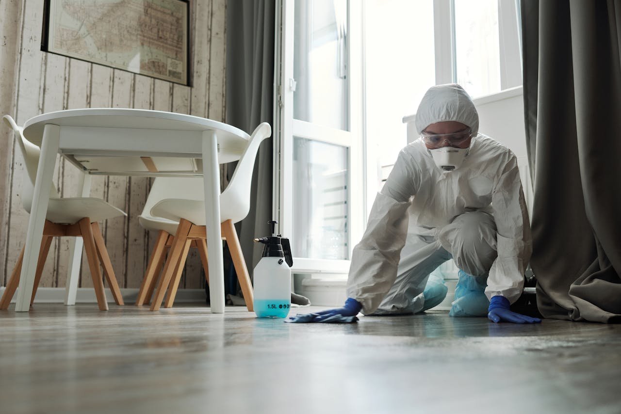 Specialized cleaning person in protective suit disinfecting a floor indoors for hygiene and safety.